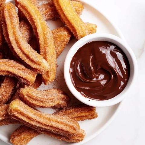 Golden-brown, crispy churros coated in cinnamon sugar, ready to be dipped into rich, dark chocolate sauce.