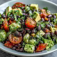 Vibrant black bean and veggie bowl with avocado, tomatoes, and lime dressing in a white bowl.