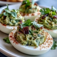 Guacamole stuffed deviled eggs with creamy avocado filling, garnished with smoked paprika and fresh cilantro.